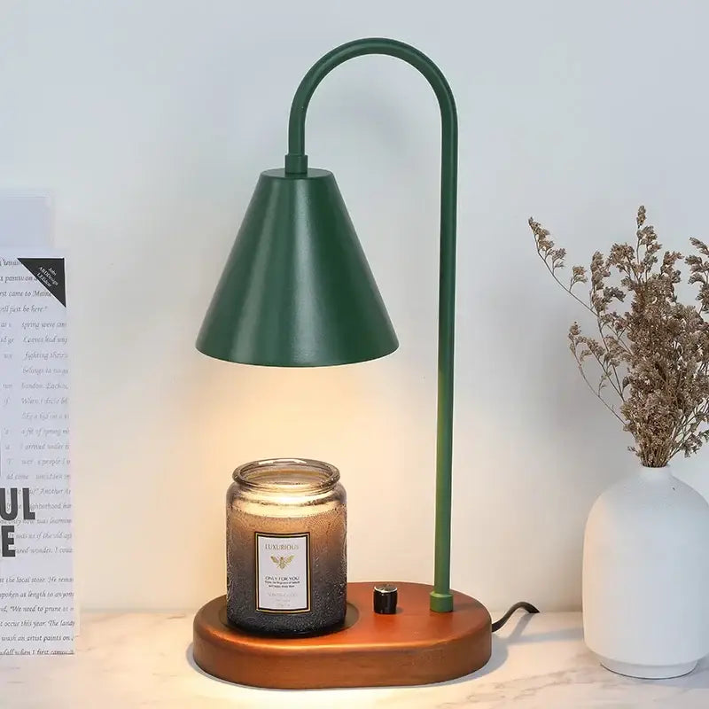 Dark green metal electric candle lamp with curved neck and wooden base beside candle jar for candle lamp warmer use