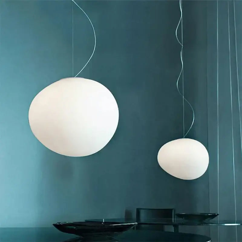 Two white matte glass pendant lights hang from silver cords against a dark teal wall by decorbites gregg glass pendant
