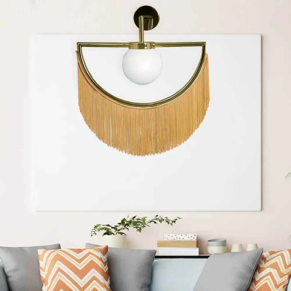 Modern matte white glass wall light with gold-toned sconce, white spherical bulb, and cascading tan fringe tassels