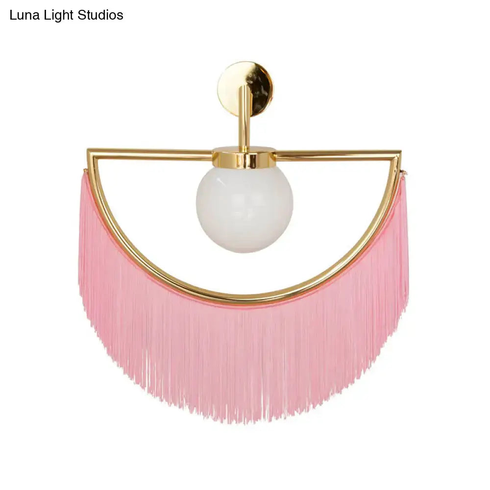 Modern matte white glass wall light with gold-toned metal frame frosted bulb and cascading pink fringe tassel sconce