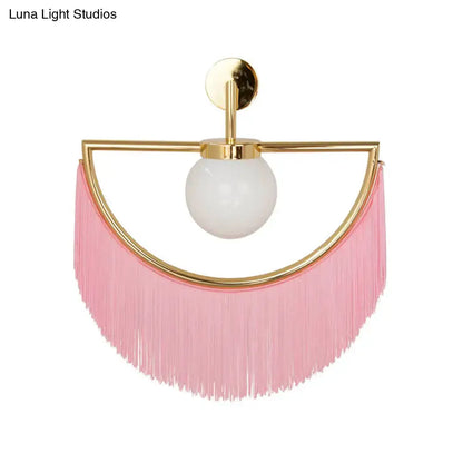 Modern matte white glass wall light with gold-toned metal frame frosted bulb and cascading pink fringe tassel sconce