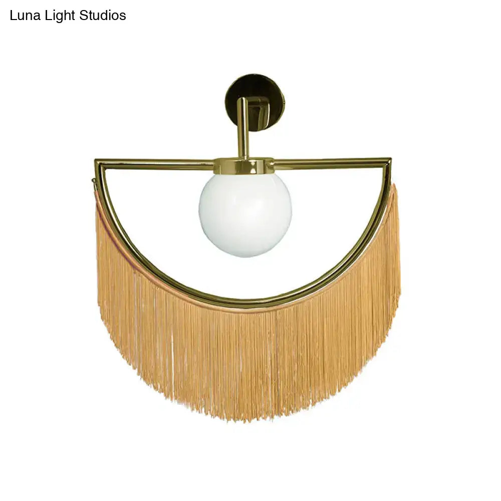 A modern matte white glass wall light with a brass semi-circular sconce and natural wood tassel fringe