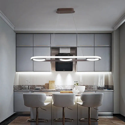 Modern metal white oval pendant light with sleek elongated design and three circular LED bulbs for kitchen island use