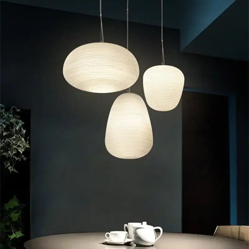 Three elegant off-white pendant lights with milky white glass whorls cocoon design hang in a dining room setting