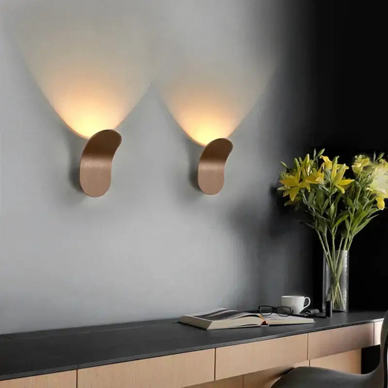 Two sleek copper led wall lights with curved leaf designs emit a warm glow in a modern minimalist bedroom setting