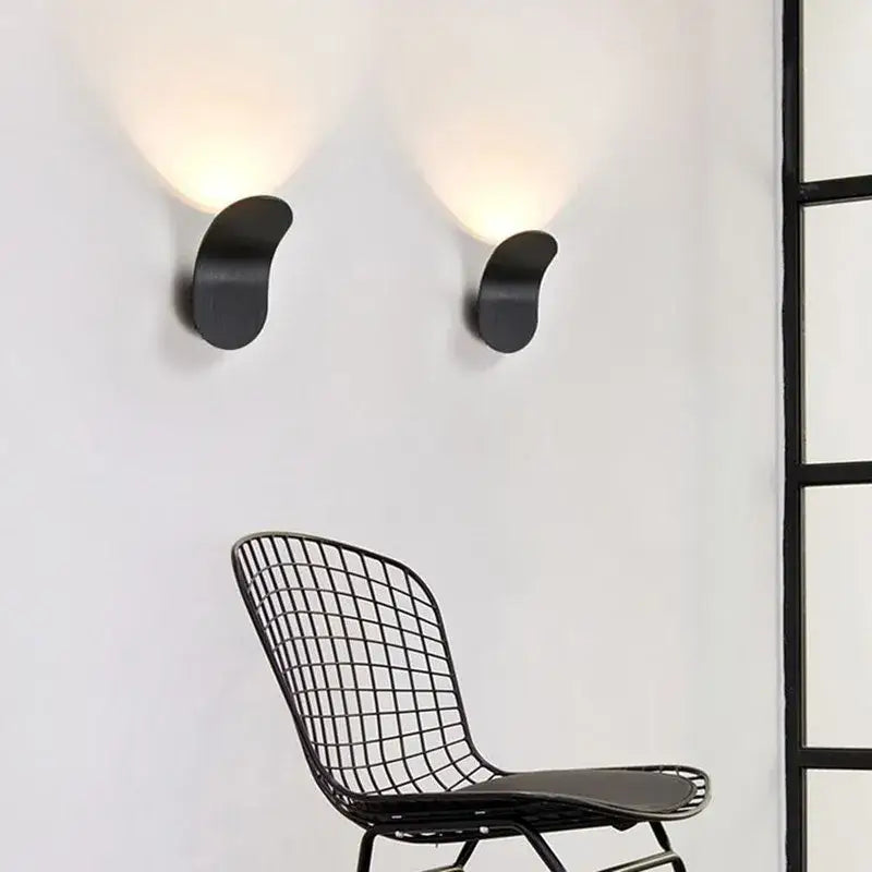 Two sleek black modern minimalist adjustable led wall lights with curved designs emit warm glow for bedroom use
