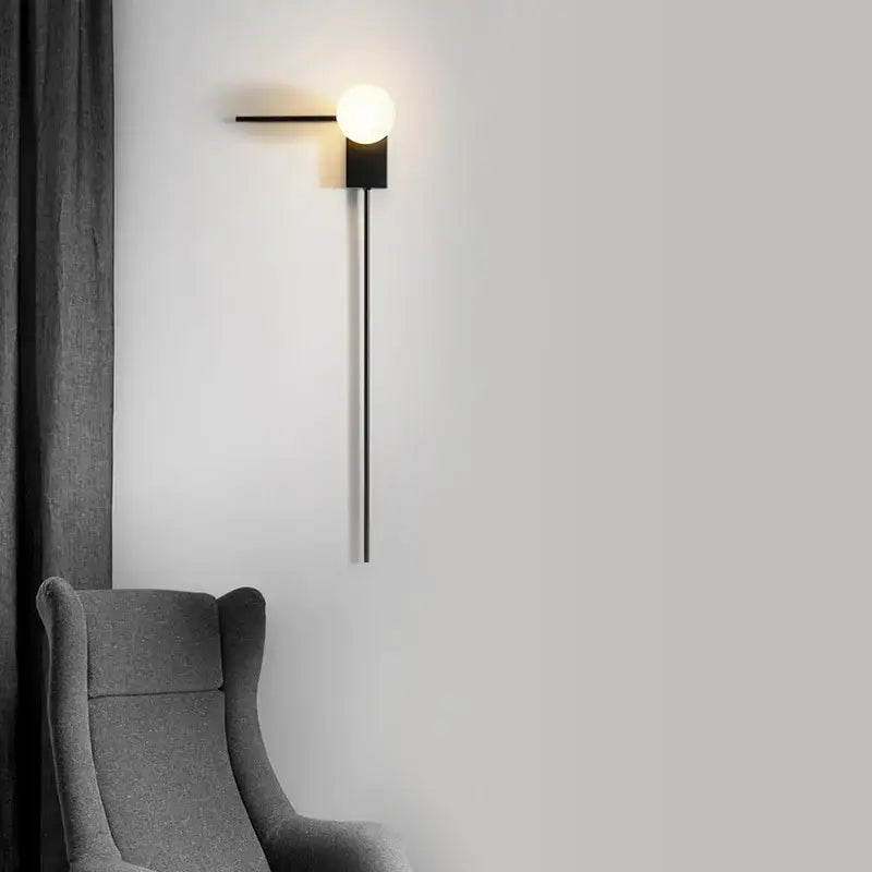 Modern minimalist black glass ball wall light with spherical frosted glass bulb and slender metal arm for bedroom use