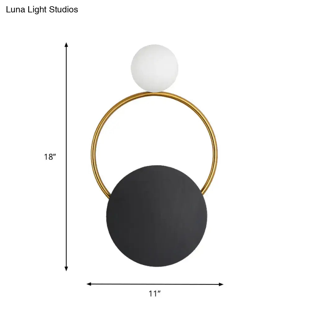 Modern minimalist black and gold wall light with a sleek gold frame, matte black disc, and white spherical lampshade