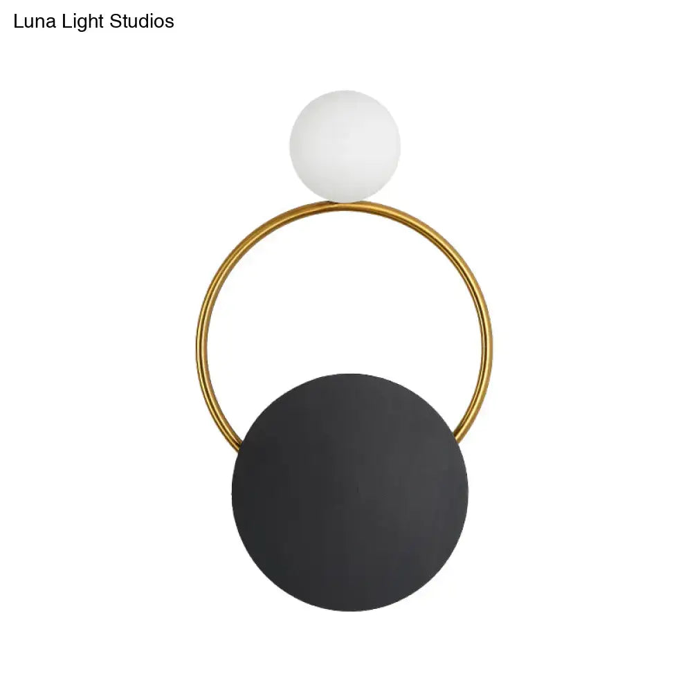 Modern minimalist black and gold wall light with a gold circular frame, matte white bulb, and large black disc for bedroom use