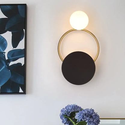 Modern minimalist black and gold wall light with a gold circular frame and two spherical shades for bedroom use