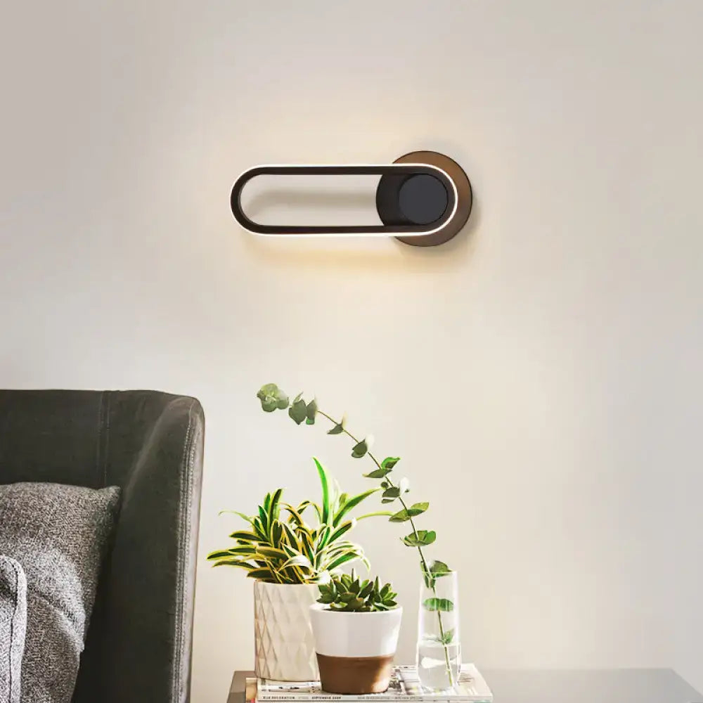 Modern minimalist black matte oval LED wall sconce with brass accents featuring a sleek design for natural colors