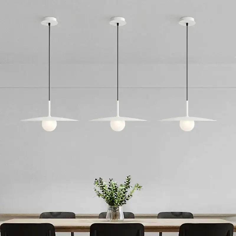 Three minimalist white pendant lights with frosted glass globes and black cords in decorbites flying saucer chandelier