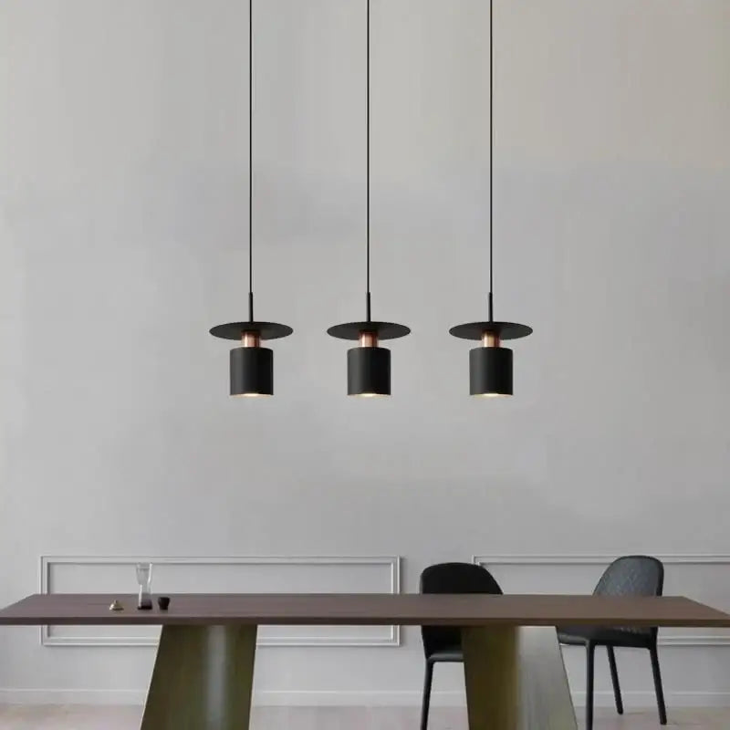 Three black and copper modern minimalist elegant led pendant lights hang above a dining table for kitchen lighting