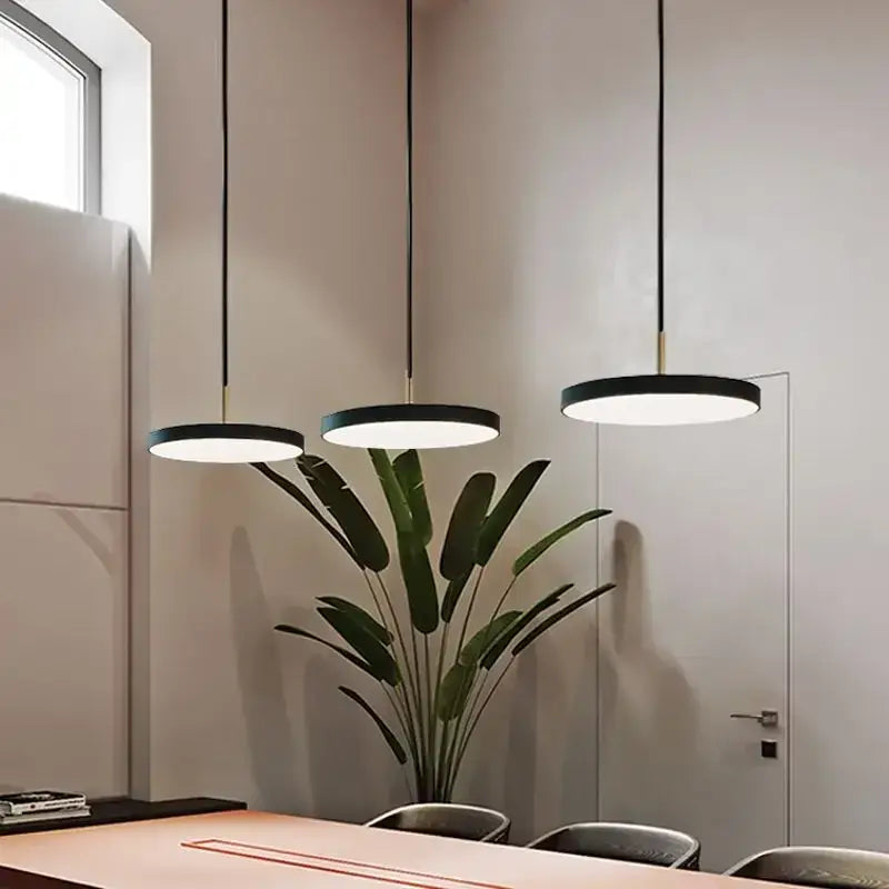 Three modern minimalist pendant lights with black shades hang above a dining table in decorbites led study disc style