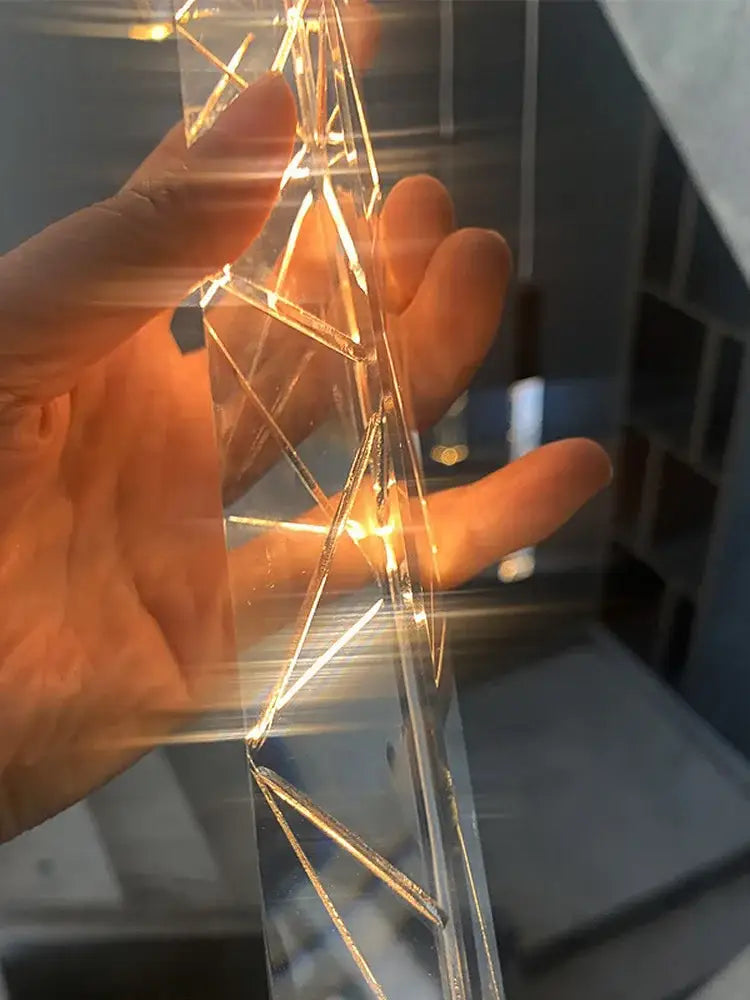 A hand holds a transparent geometrically structured crystal chrome led light string with warm golden filaments decorbites crystal chrome