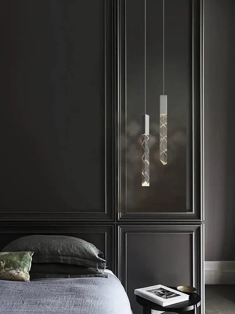 Two minimalist decorbites crystal chrome led pendant lights with geometric glass shades hang against a dark paneled wall