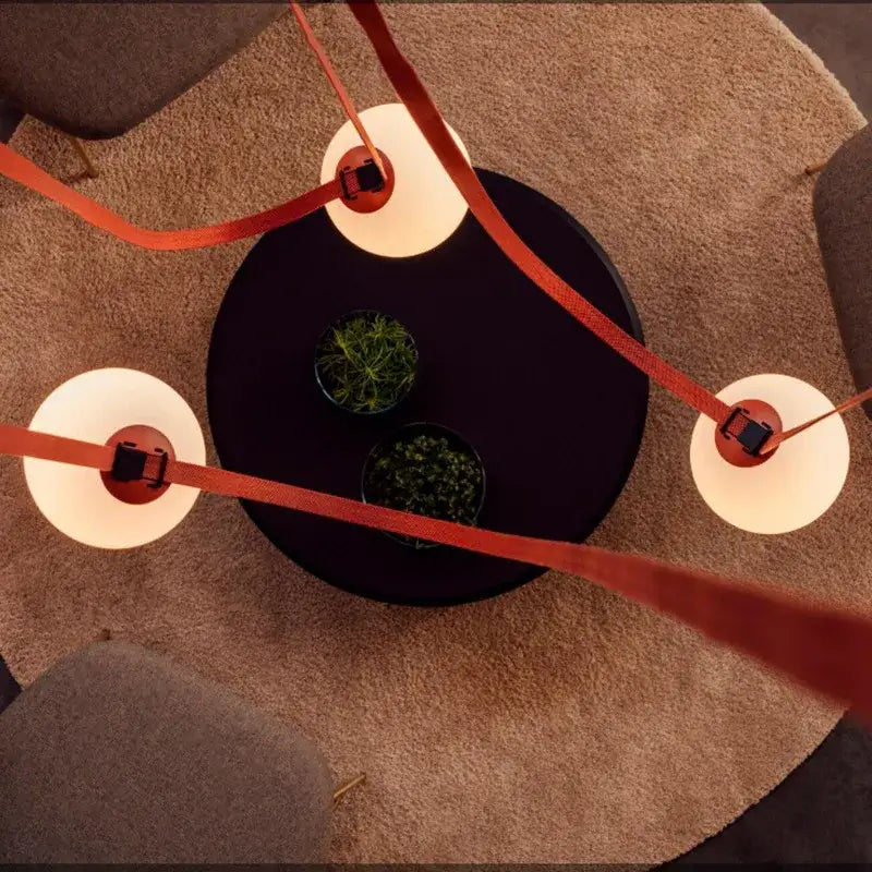 Modern minimalist black round coffee table with three frosted glass ball pendant lights suspended by orange ribbons