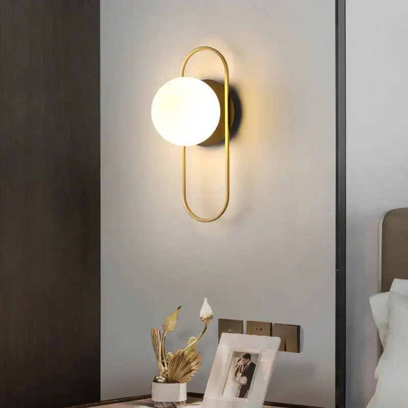 Gold-toned modern minimalist led wall lamp with curved metal frame and frosted glass globe for bedroom sconce lighting