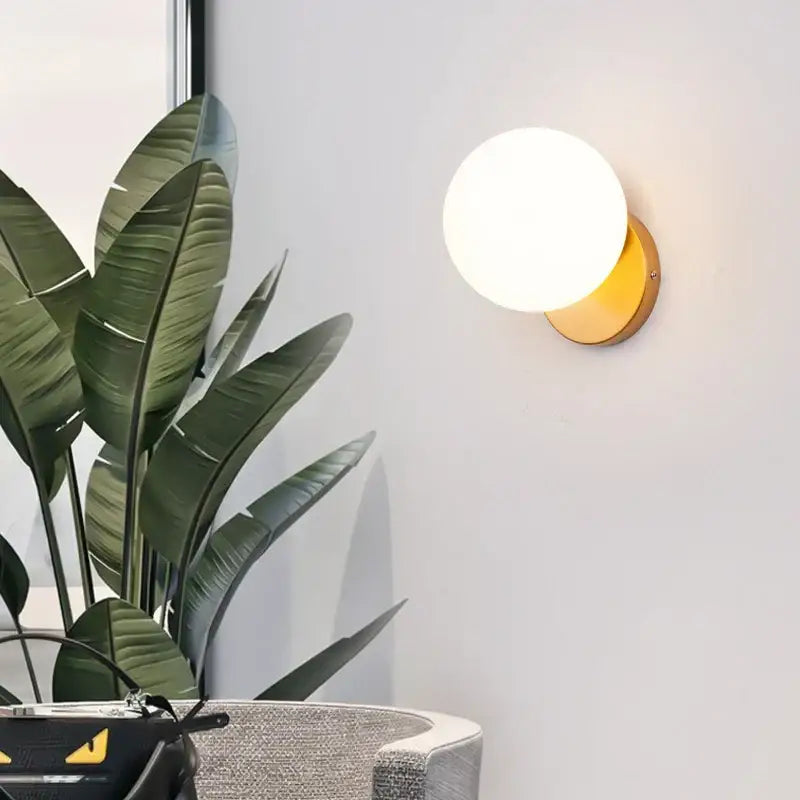 A modern minimalist led wall lamp with a frosted white glass ball shade and warm gold metal base for bedroom use