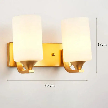 Modern minimalist wall lamp with gold finish and two cylindrical frosted glass shades for bedroom use