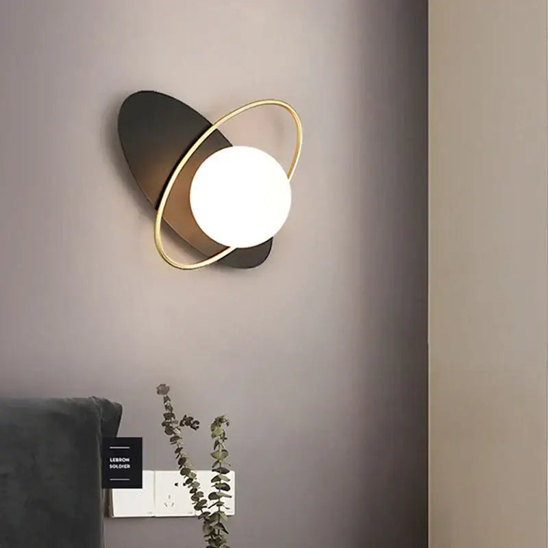 Modern minimalist wall lamp with a glowing white glass gold led bulb encircled by a gold ring on a black base decorbites glass gold
