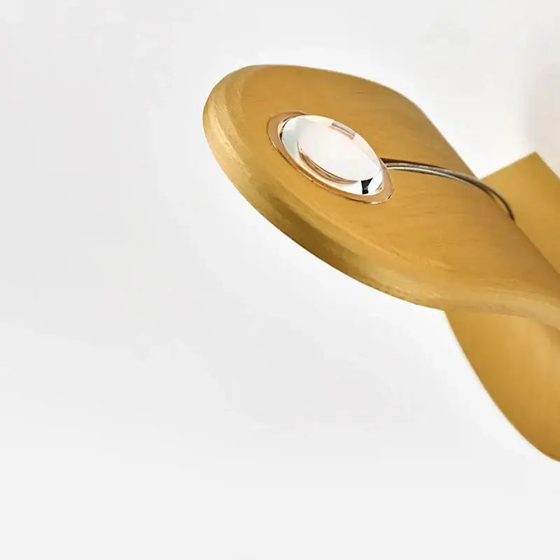 A sleek light wood spoon with polished metallic ring and glass accent shown alongside modern minimalist led wall lamps