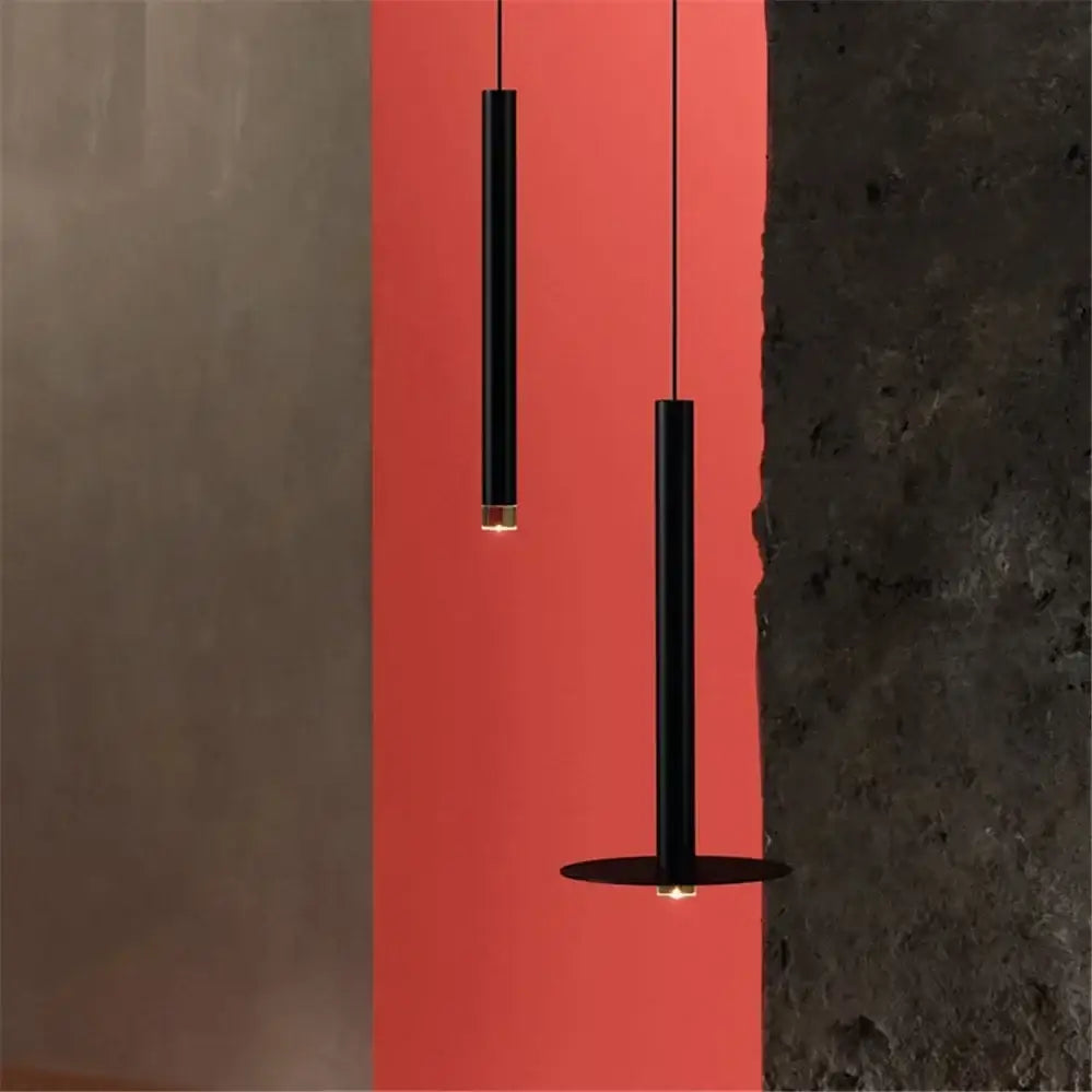 Two minimalist black cylindrical pendant lights with gold tube led accents against a vibrant red wall for kitchen decorbites gold tube