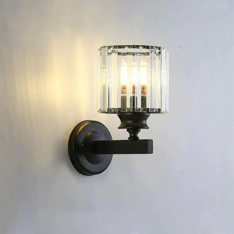 Black metal modern minimalist wall lamp with cylindrical crystal glass shade housing three exposed bulbs for bedroom