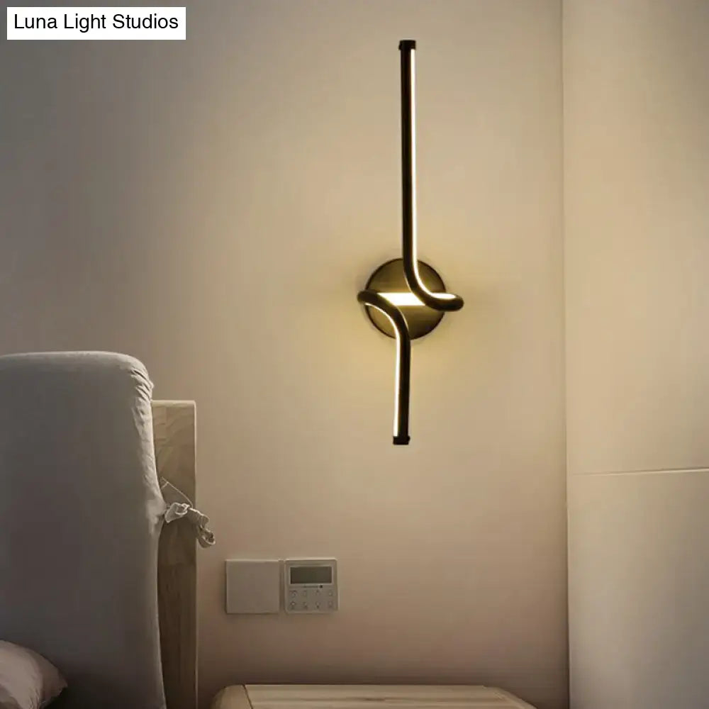 Modern minimalist gold-toned metallic led wall sconce with sleek curved arm and circular base for bedroom lighting