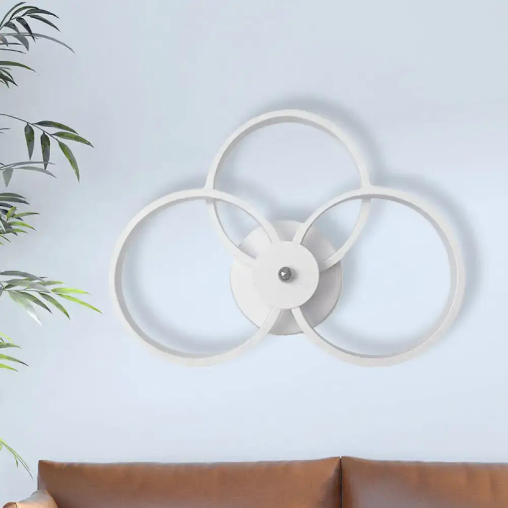 Modern minimalist white wall sconce light with three interlocking rings and central metallic accent for bedroom use