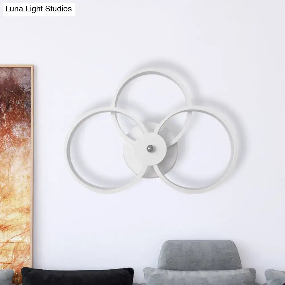 Modern minimalist white wall sconce light with three interlocking rings and central metallic accent for bedroom use