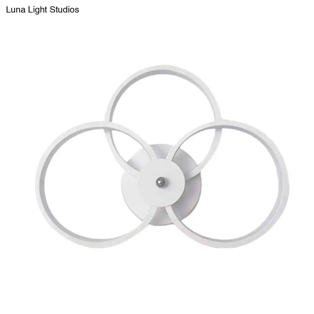 Modern minimalist white wall sconce light featuring three interlocking circular LED rings for bedroom illumination