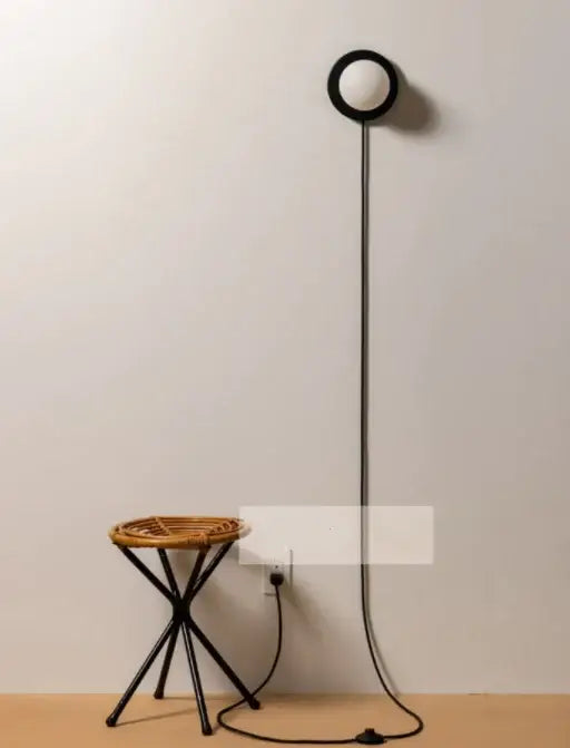 Black circular floor lamp with slender pole and cord paired with modern minimalist white frosted glass ball wall light bedroom sconce