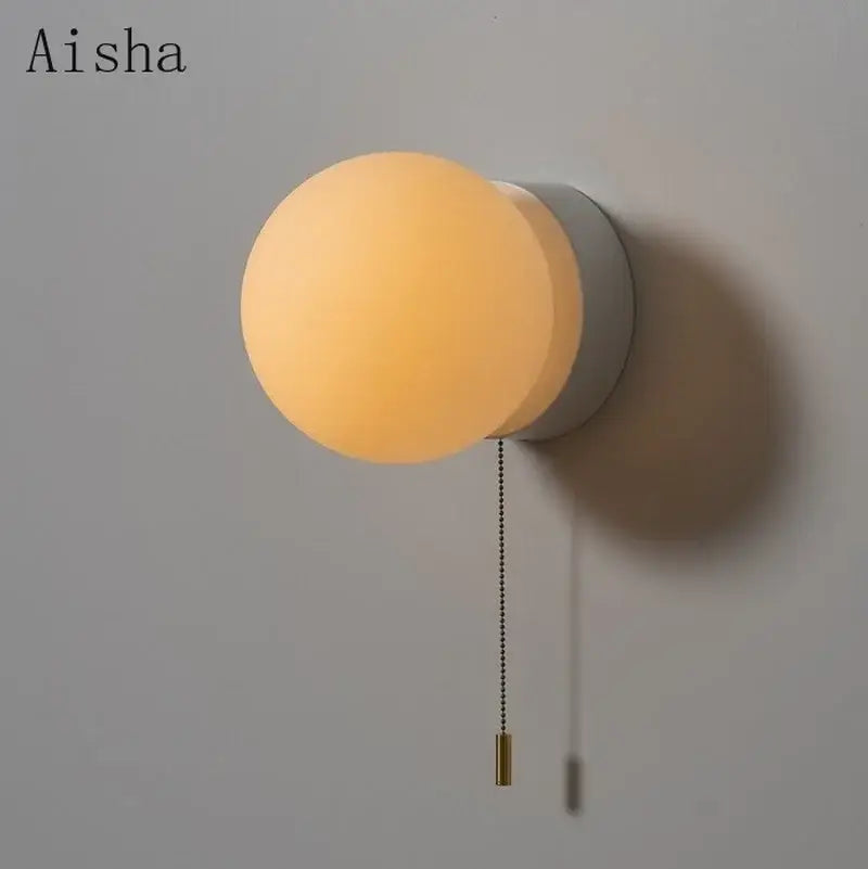 Aisha brand modern minimalist ball wall light with warm amber glass globe, matte gray base, and brass pull chain wall light
