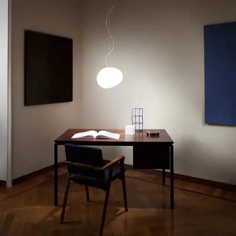 A sleek white glass ball led pendant light with a thin cord hangs above a dark wooden desk for modern decorbites pendant lights