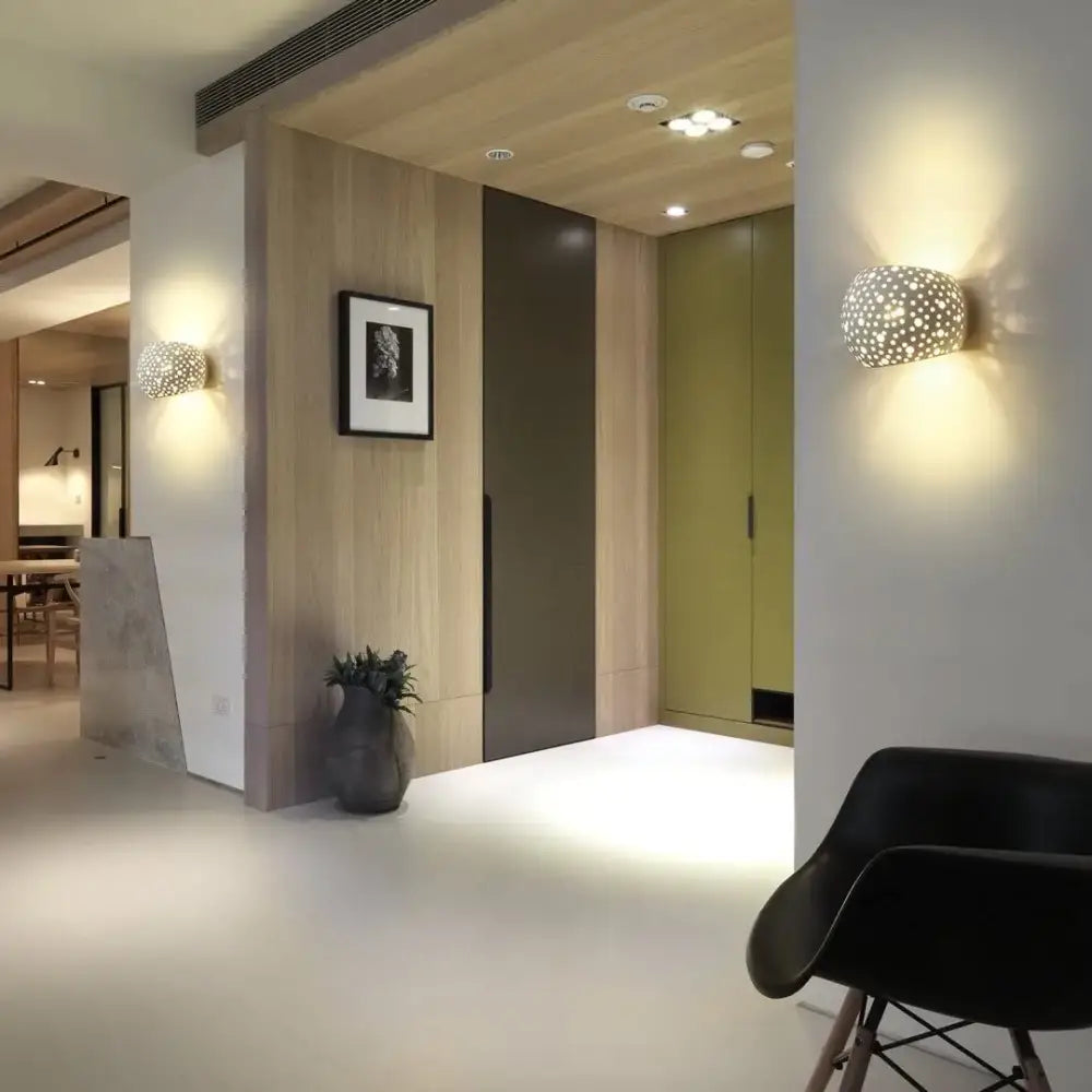 Modern minimalist white gypsum led wall lamp with spherical perforated matte surface and warm ambient lighting