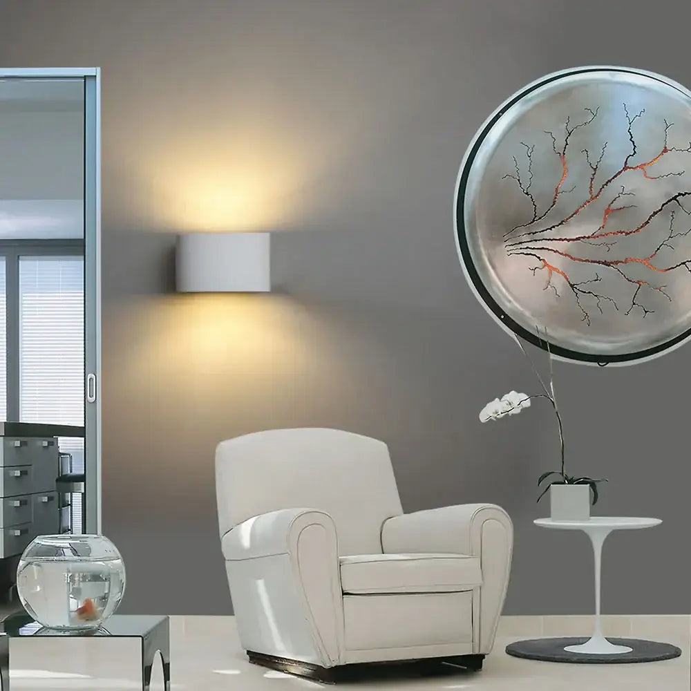 White leather armchair with curved arms and cushioned seat next to modern minimalist white gypsum led wall lamp for bedroom lighting