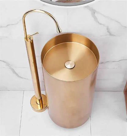 Gold-toned cylindrical pedestal sink with matching tall faucet and modern minimalist white standing bathtub faucet curved spout