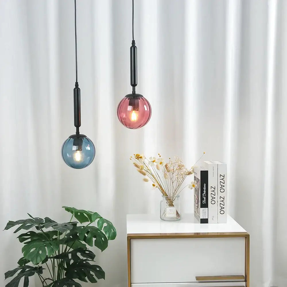 Two glass pendant lights in blue and pink with painted iron finish hanging by black cords for dining room