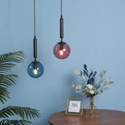 Two spherical glass pendant lights in translucent blue and pinkish-purple shades with painted iron rods for dining rooms