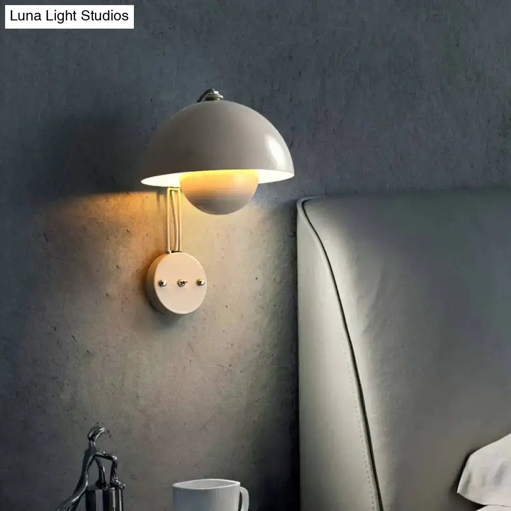 A sleek matte white wall lamp with a dome-shaped shade and brass base type finish for modern bedroom use