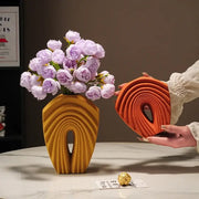 A modern mustard yellow geometric folds ceramic vase with sculpted arch design holds light purple roses for decorbites decor
