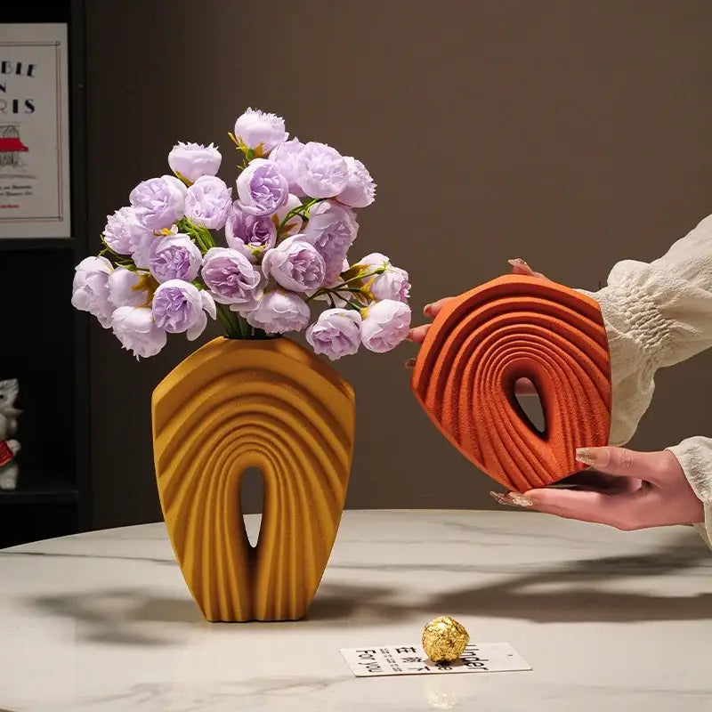 A modern mustard yellow geometric folds ceramic vase with sculpted arch design holds light purple roses for decorbites decor