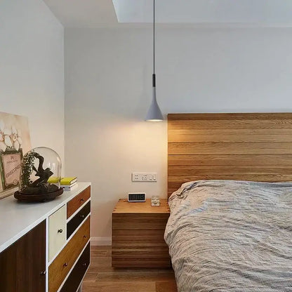 Modern nordic pendant light with sleek gray conical shade and black metal cord hanging above the bed