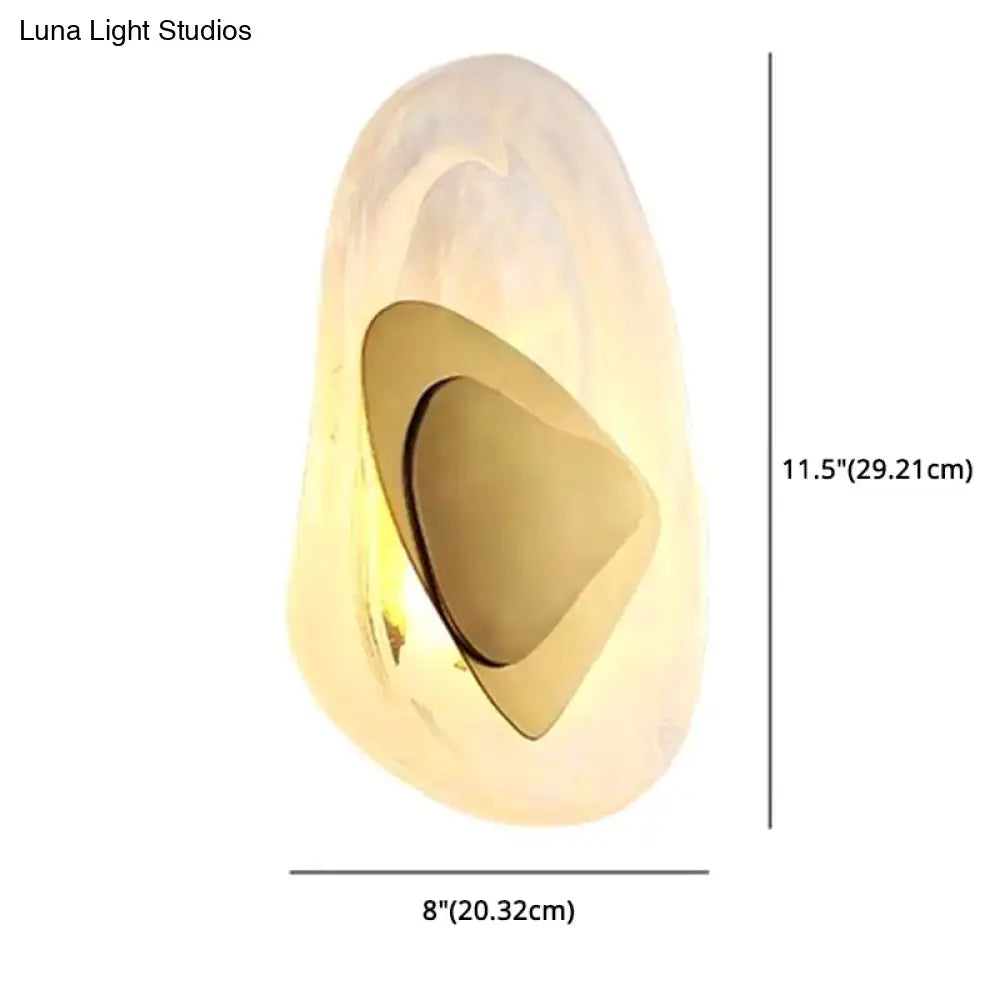 A modern nordic sconce light fixture with a translucent white shell and polished gold geometric cutout for bedroom use