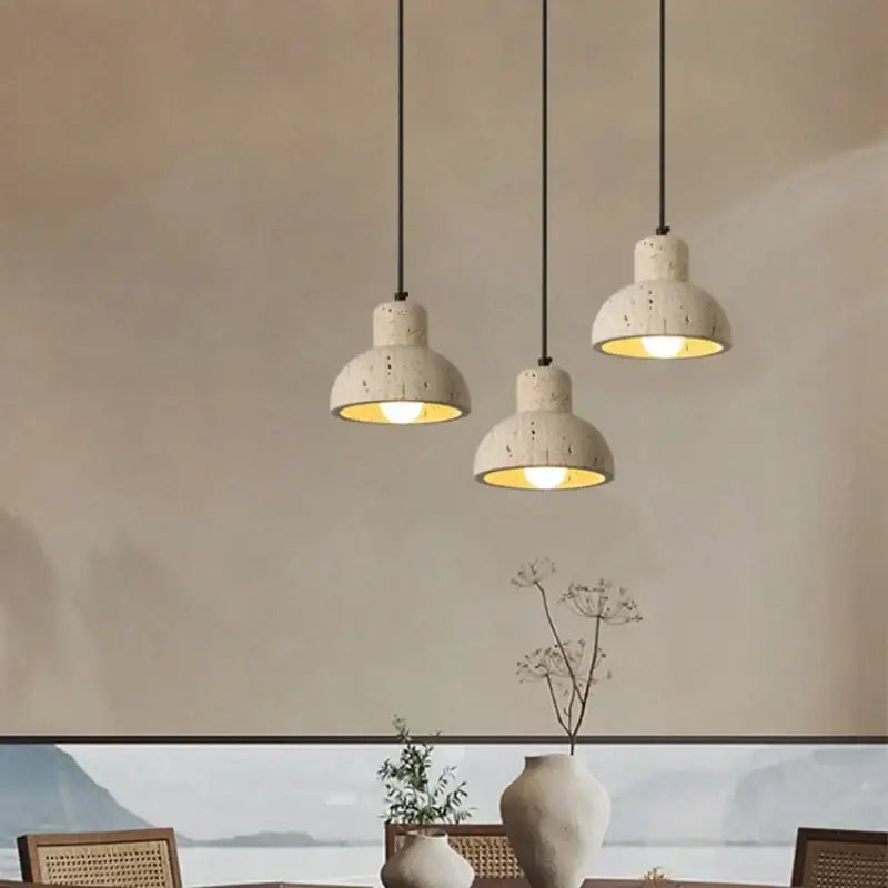Three minimalist decorbites cave stone led pendant lights with speckled off white ceramic shades hang above dining area