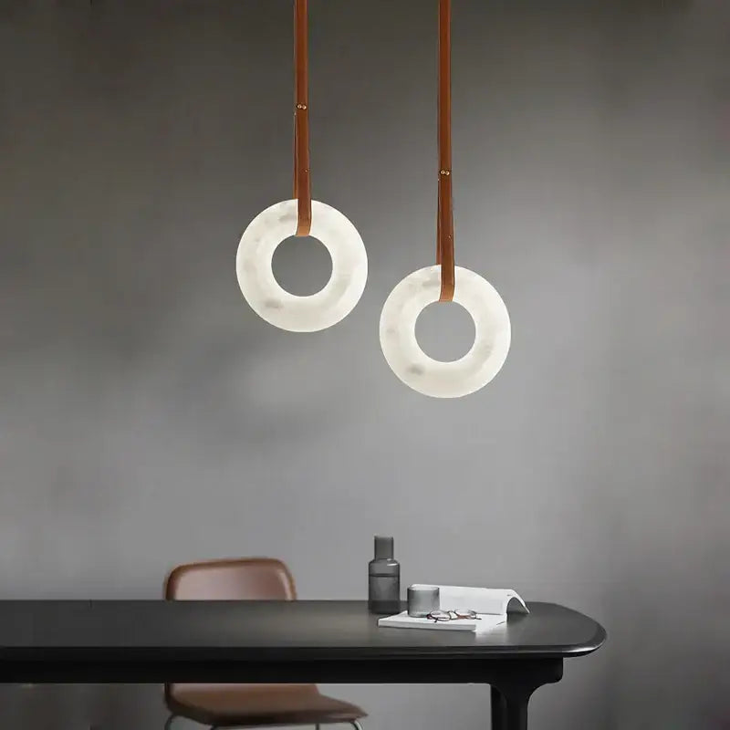 Two minimalist modern opal glass ring marble chandelier pendant lights with translucent white shades and brown leather straps