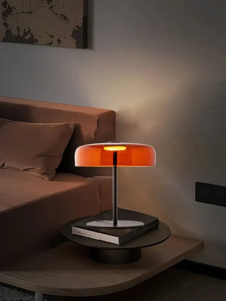 A sleek modern glass table lamp with a translucent orange shade and slender metallic base for bedroom decorbites glass table