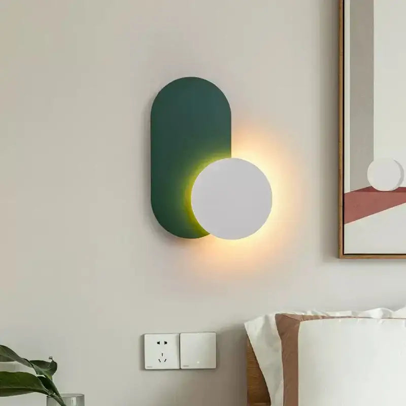 Modern orange and white decorbites led wall light with matte dark green oval and white circular fixture emitting warm glow