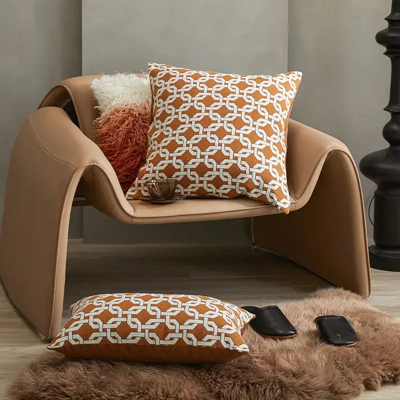 Tan leather armchair with curved modern design and geometric orange jacquard crochet pillow cover by decorbites